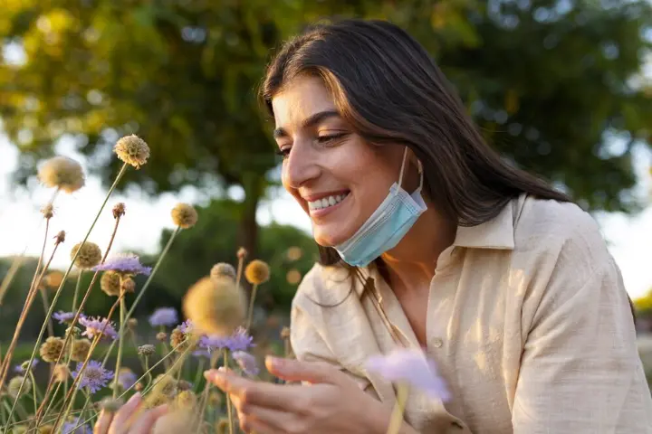 Alergia estacional: chica con mascarilla oliendo unas flores