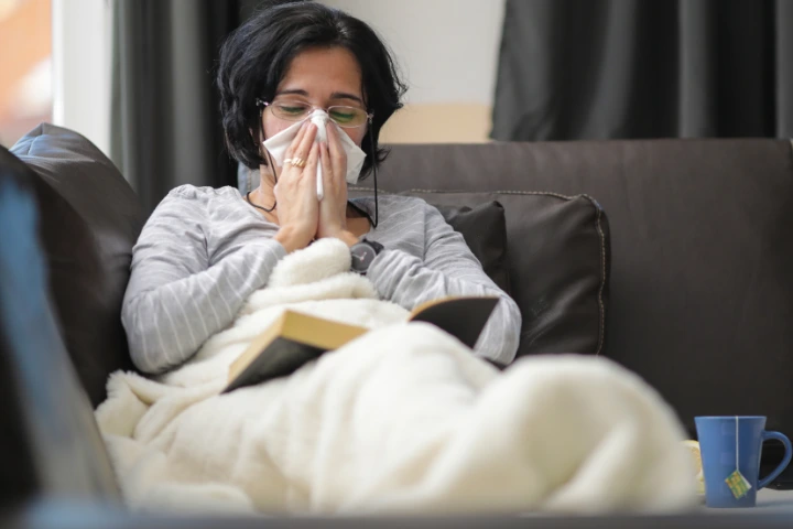 por que nos resfriamos en invierno: mujer sonandose los mocos resfriada en el sofá tapada con una manta